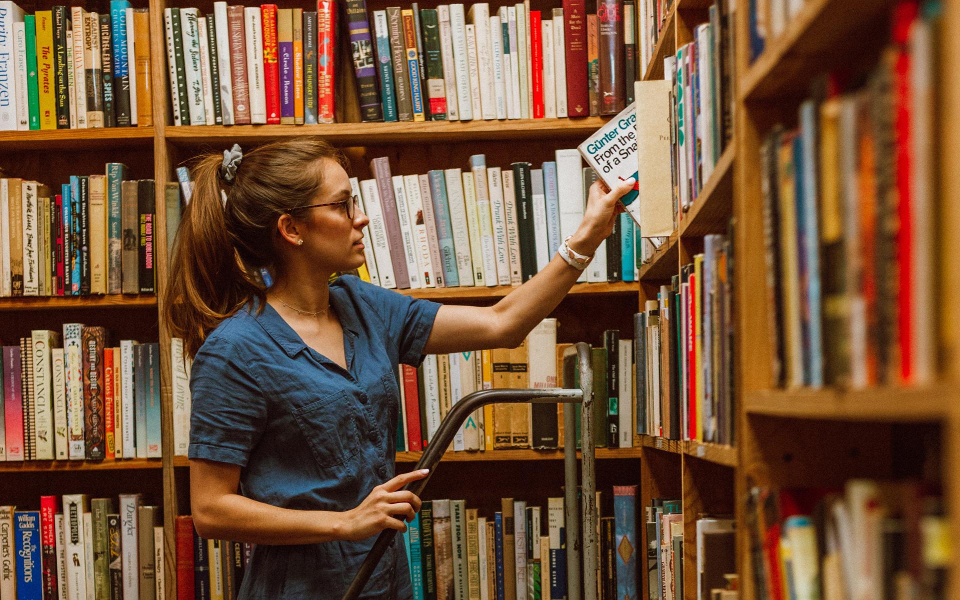 Junge Frau auf einer Leiter vor dem Bücherregal